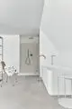 Weißer Badezimmerbereich mit einer Dusche, ausgestattet mit einer runden Kopfbrause von Ideal Standard, und einer freistehenden Badewanne. Ein Stuhl mit gefalteten Handtüchern ist sichtbar.